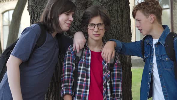 Classmates Teasing Nerd Caucasian Boy on Schoolyard. Portrait of Brunette Scared Schoolboy in