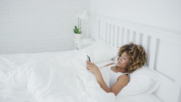 Smiling Woman Relaxing with Phone in Bed