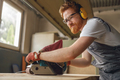 Bearded male wood worker using electric sander for wood. Carpentry workshop. High quality photo - PhotoDune Item for Sale