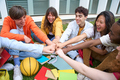Diverse young friends gathered in circle sitting on campus excited fist bumping. Multi-ethnic group. - PhotoDune Item for Sale