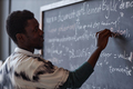 Teacher writing on blackboard in the classroom - PhotoDune Item for Sale