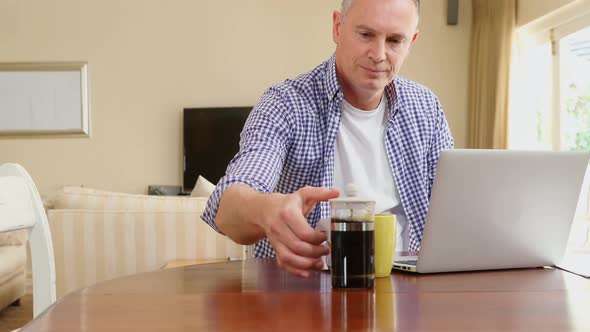 Mature man using laptop while having coffee 