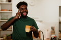 A cheerful interracial man is standing in a kitchen at home and talking on the phone - PhotoDune Item for Sale
