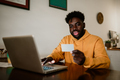 An African American man is sitting at home and shopping online on his laptop. - PhotoDune Item for Sale