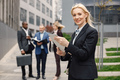 Blonde businesswoman standing and using a tablet in front of modern office - PhotoDune Item for Sale