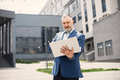 Bearded man standing and using a laptop in front of modern office - PhotoDune Item for Sale