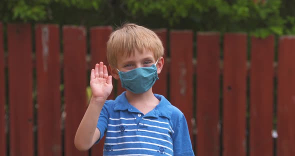 Cute little boy waving while wearing a protective face mask.