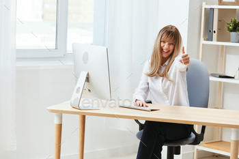  freelancer look at camera show thumb up gesture in light modern office. Employee work on computer online enjoy successful career. Copy space