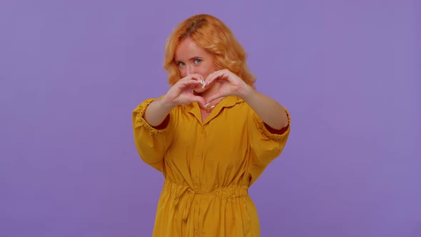 Smiling Redhead Girl Makes Heart Gesture Demonstrates Love Sign Expresses Good Feelings and Sympathy