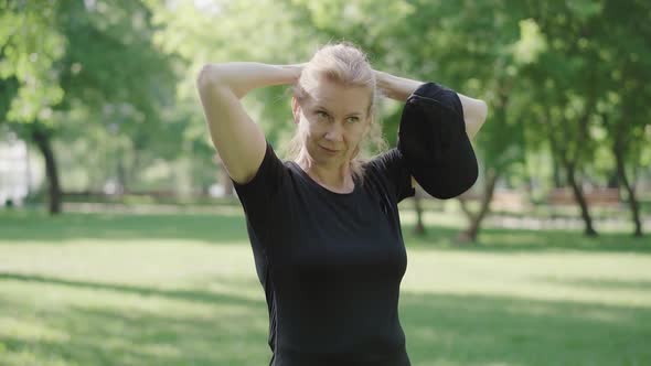 Confident Mid-adult Woman Making Ponytail and Putting on Cap. Portrait of Athletic Caucasian Lady