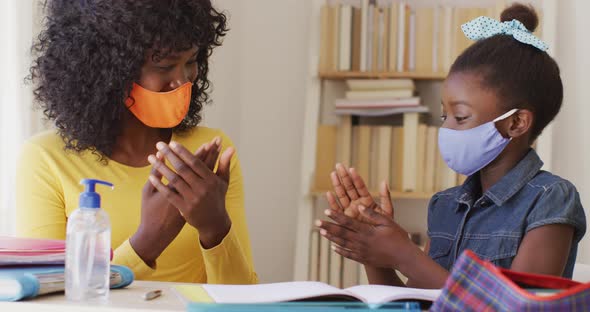 African american mother and daughter wearing face mask sanitizing their hands at home