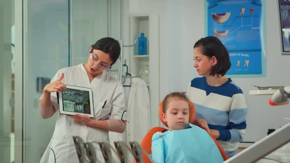 Pediatric Dentist Showing Teeth Xray on Tablet Pc Computer Screen To Mother