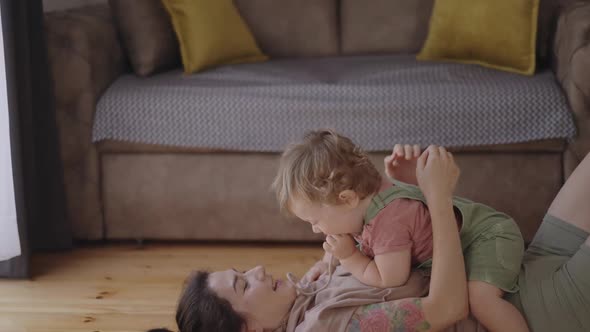 Happy Carefree Mother and Cute Small Child Daughter Tickling Laughing Having Fun Lying on Sofa and