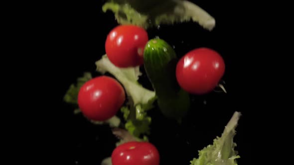 Fresh Tomatoes Cucumbers and Lettuce Tossed Up and Spinning with Water Splashes on a Black