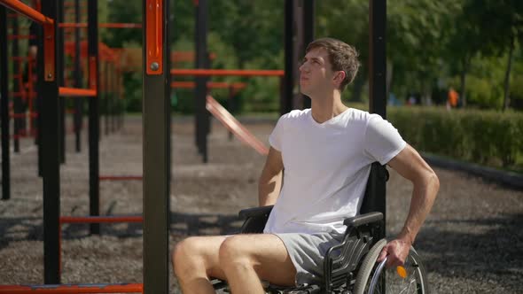 Motivated Sportsman in Wheelchair on Sports Ground in Park Touching Fitness Equipment in Slow Motion