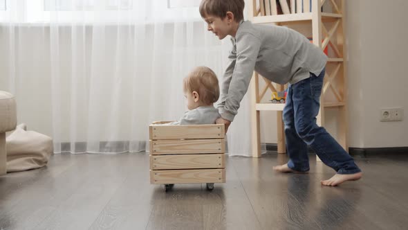 Older boy riding his baby brother in wooden toy cart