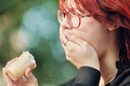Red-haired teenage girl with glasses eats ice cream. Sensitive teeth, cold food, toothache. - PhotoDune Item for Sale