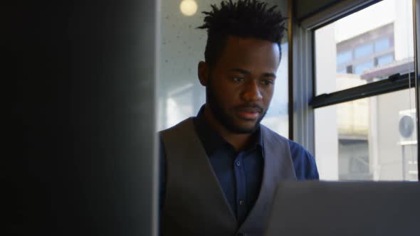 Front view of young black businessman working on laptop at desk in a modern office 4k