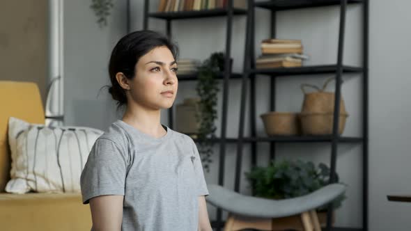 Young Asian Woman Sitting On The Floor Looking Away With A Thoughtful Look, Is in A Cozy Room