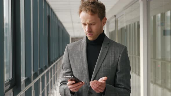 Close up of young handsome businessman walking indoor. Looking at his Smartphone Screen. Uses his ph