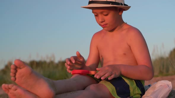 Boy is Playing Pop It Sitting on the Beach Under the Setting Sun