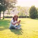 A Young Woman Uses Her Phone While Sitting on a Green Bright Lawn - VideoHive Item for Sale