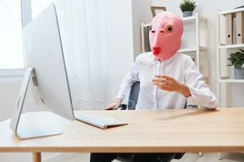 r in pink fish mask work on computer online pondering or making decision thinking of problem solution in light modern office. Copy space