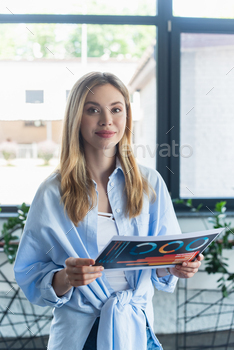 Young businesswoman smiling at camera while holding paper in office