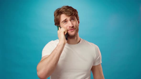 Young Man in White Shirt Cheerfully Talking on the Phone Against Blue Background