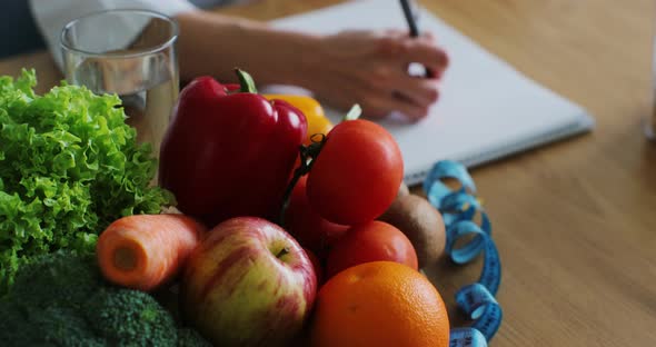 Close Up of Nutritionist Woman Writing Diet Plan on Table Full of Fruits and Vegetables