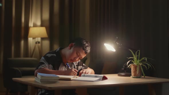 Asian Boy Is Studying At Home, Asia Child Writing While Sitting On The Table At Night