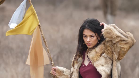 Vmestizo young woman in ethnic clothes with a stick with rags in the steppe in nature. Slow mo