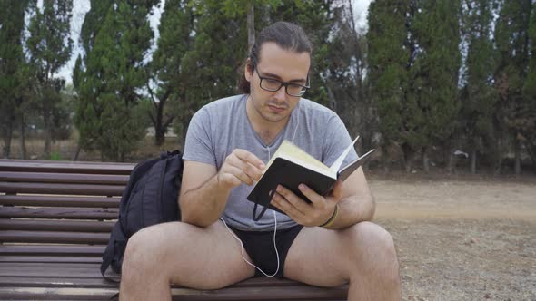 A long haired man sitting and reading in a park