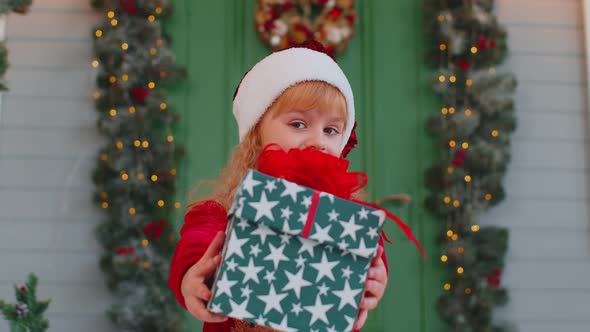 Happy Toddler Child Girl Kid in Red Sweater Presenting One Christmas Gift Box Stretches Out Hands