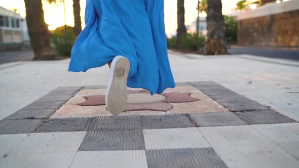 Legs of a Woman in a Beautiful Blue Dress Running Along the Palm Avenue