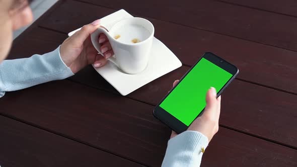 Womans Hand Use Green Screen Smartphone for Online Shopping at Cafe Table with Coffee Cup