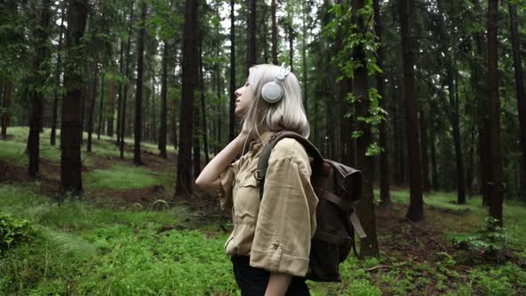 Blond hair woman in headphones with backpack in rainy forest