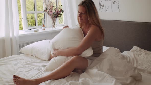 Woman Sitting On Bed Hugging Pillow In Morning