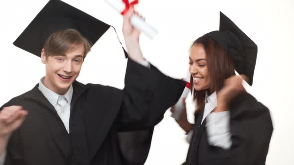Caucasian Young Graduate Male Happily Dancing and Rejoicing with African American Female in Black