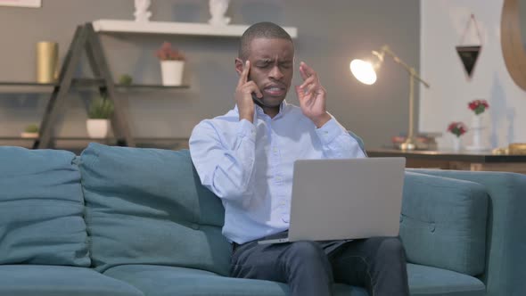 African Man with Laptop Having Headache on Sofa