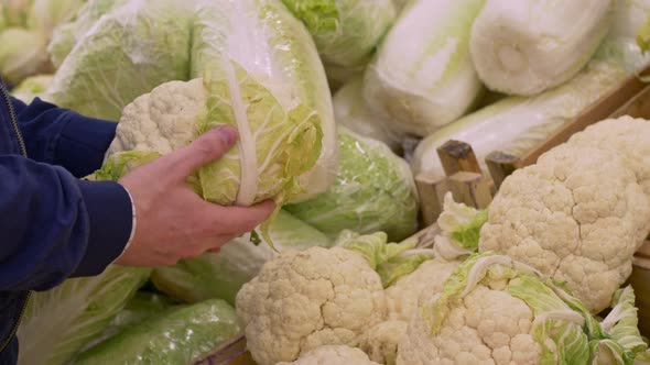 A Man Buys Fresh Cauliflower at a Farmer's Fair Picks Up a Head of White Cauliflower From a Shelf