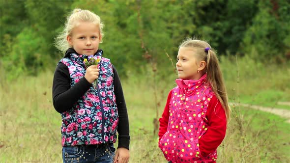 Two beautiful little girls happily sniffing a bouquet of wild flowers outdoors