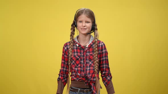 Positive Caucasian Teenage Girl in Headphones with Microphone Talking Gesturing at Yellow Background