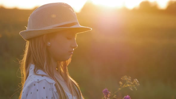A Pretty Girl in Hat Enjoys Wildflowers at Sunset.