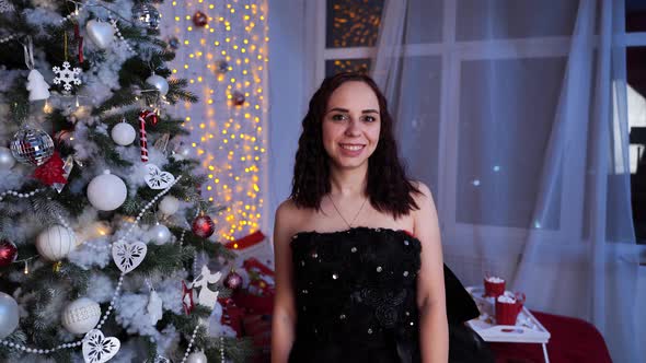 Portrait of Charming Brunette in Black Dress Near Christmas Tree