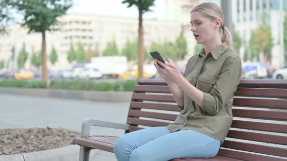 Woman Reacting to Loss on Smartphone while Sitting Outdoor on Bench