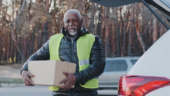 Mature African American Male Loader Worker in Uniform Outdoors Standing Near Car Holding Cardboard