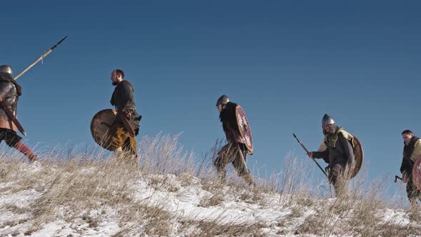 Group of Vikings with Shields and Swords Going Forward on the Winter Meadow