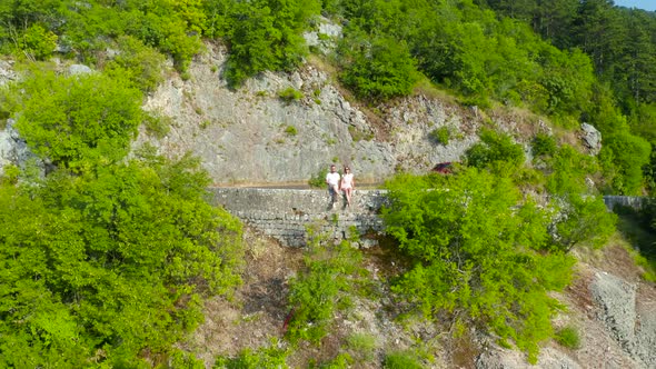 A Couple of a Man and a Woman are Sitting on the Edge of a Serpentine Road in the Bay of Kotor