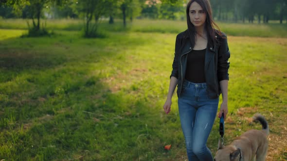 Frontal Wide View of a Young Woman in Jeans and Leather Jacket Leading Her Dog for a Walk.